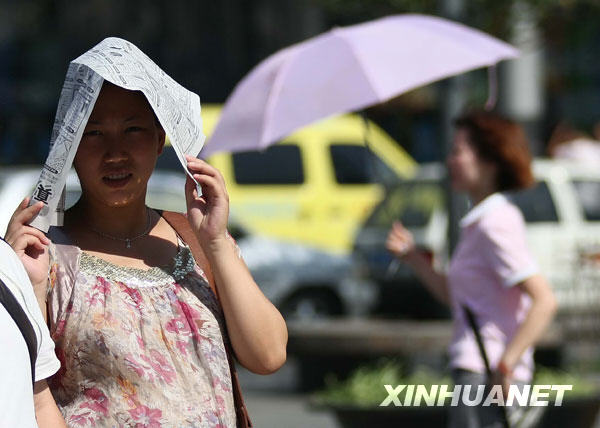 6月24日，一名郑州市民在街头用报纸遮挡烈日。